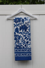 Load image into Gallery viewer, Blue floral patterned tablecloth on a white hanger against a white wooden background